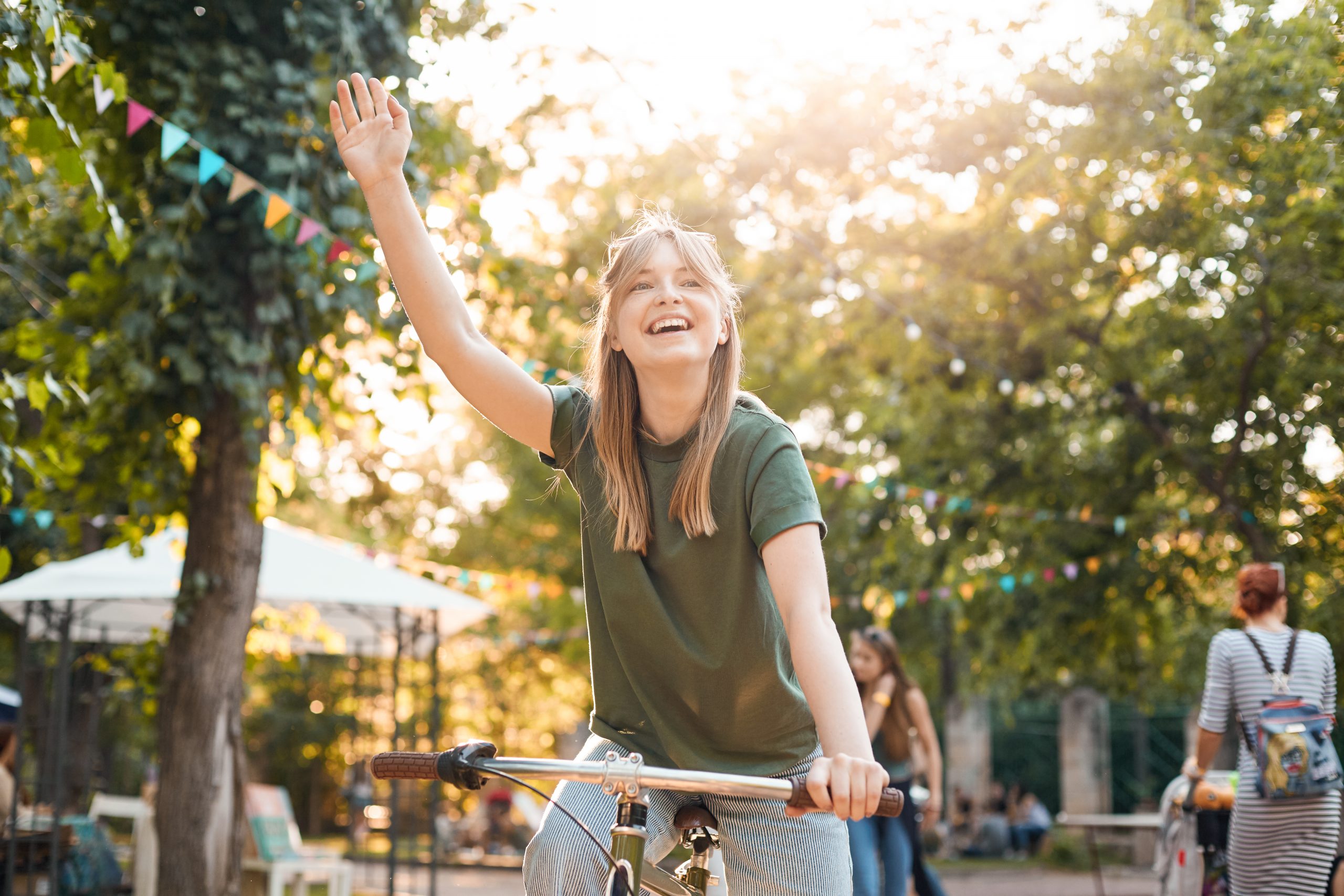 Girl riding bike in park. Portrait of a young female riding a bycicle outdoors and waving her friends or boyfriend smiling. Healthy lifestyle concept.